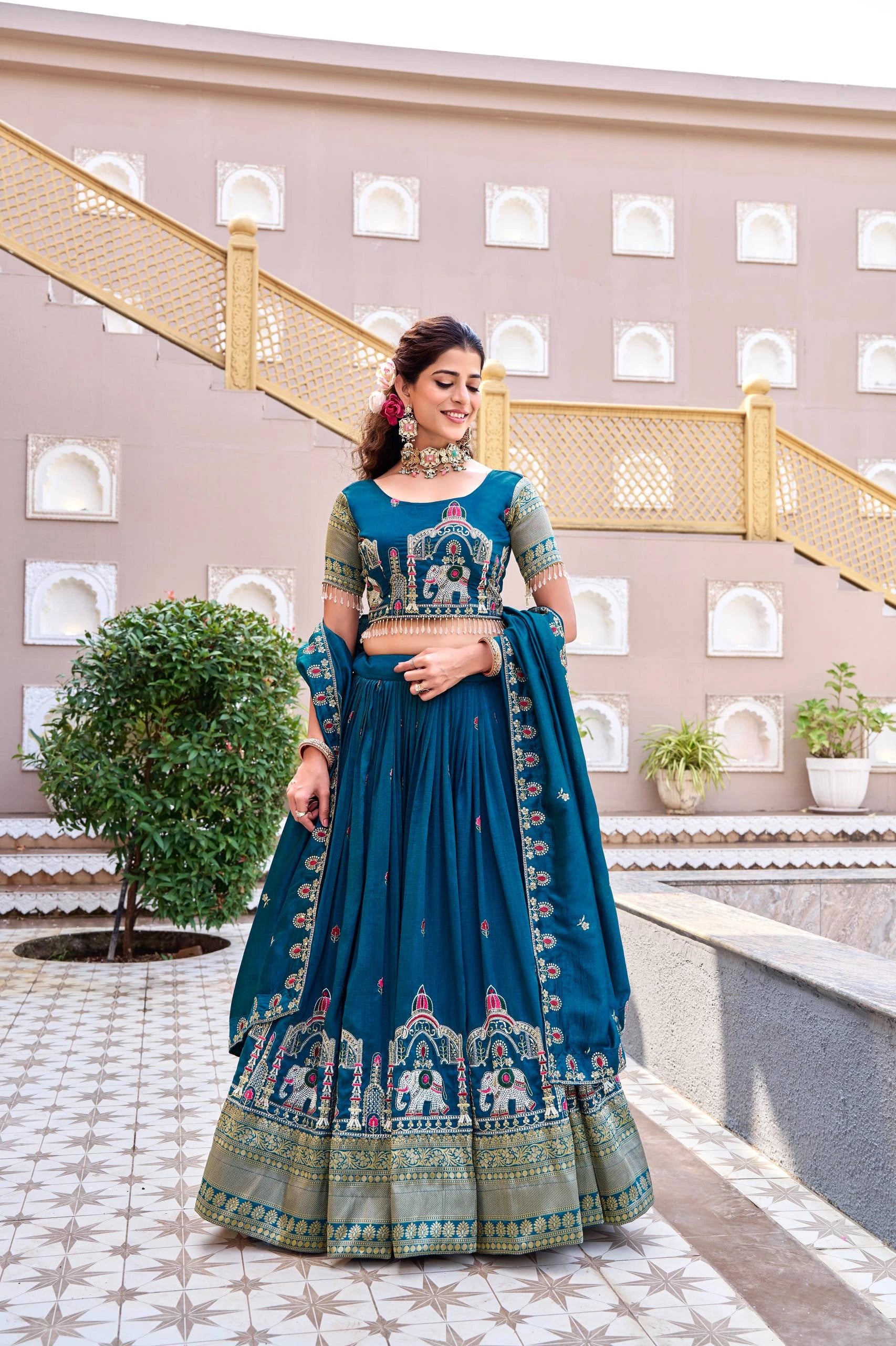 Woman in a traditional blue embroidered outfit standing in front of a decorative building.